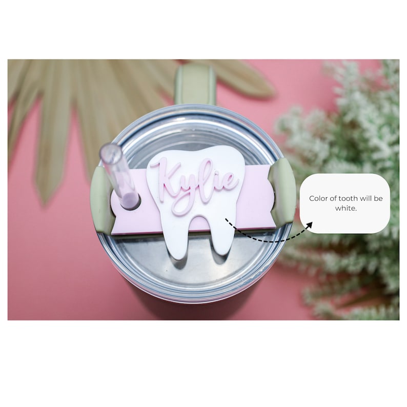 May include: A pink and white tooth-shaped tumbler lid with the name "Kylie" written on it. The tooth is white and the name is pink.