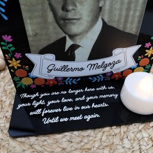 May include: A black acrylic memorial plaque featuring a portrait of Guillermo Melgoza, a white banner with his name, colorful floral accents, and the text: Though you are no longer here with us, your light, your love, and your memory will forever live in our hearts. Until we meet again. A white LED tea light sits on the base.