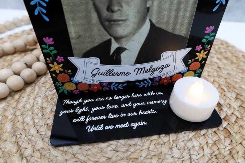 May include: A black acrylic memorial plaque featuring a portrait of Guillermo Melgoza, a white banner with his name, colorful floral accents, and the text: Though you are no longer here with us, your light, your love, and your memory will forever live in our hearts. Until we meet again. A white LED tea light sits on the base.