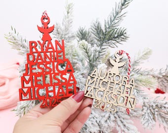 May include: Two wooden Christmas ornaments. One is red and the other is natural wood. Both ornaments are shaped like Christmas trees and feature names and the year 2025. Each ornament has a small angel at the top.