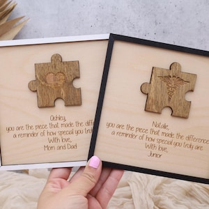 May include: Two wooden framed signs with a puzzle piece design. The top sign reads "Oshley, you are the piece that made the difference, a reminder of how special you truly are. With love, Mom and Dad." The bottom sign reads "Natale, you are the piece that made the difference, a reminder of how special you truly are. With love, Junior."