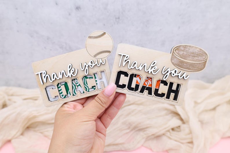 May include: Two wooden gift card holders with the words "Thank you COACH" in white script. One has a baseball graphic, the other a hockey puck. The word COACH is in green and black, and black and orange.