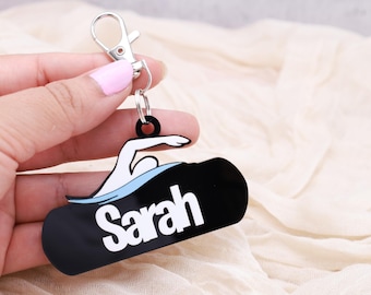 May include: Black and white swimmer keychain with the name "Sarah" on a black background.