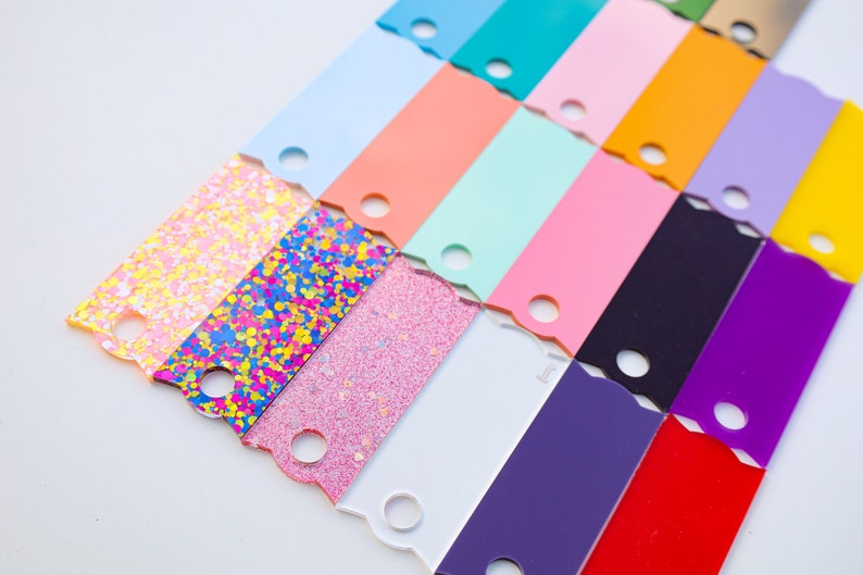 May include: A collection of colorful acrylic sheets with a scalloped edge and a hole in the center. The sheets are arranged in a staggered pattern, with the glitter sheets at the bottom.