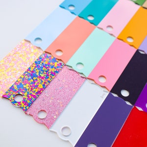May include: A collection of colorful acrylic sheets with a scalloped edge and a hole in the center. The sheets are arranged in a staggered pattern, with the glitter sheets at the bottom.