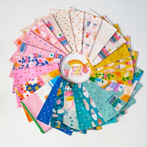 May include: A circular arrangement of colorful fabric squares with various patterns, including ice cream cones, typewriters, and floral designs. The center features a button with the text "BEST DAY EVER" and a rainbow. The fabrics are in shades of pink, blue, yellow, and green.