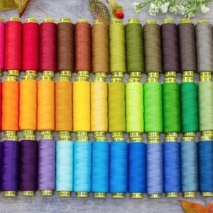 May include: A rainbow assortment of spools of thread, arranged in rows of different colors. The thread is wound around spools with yellow plastic caps.