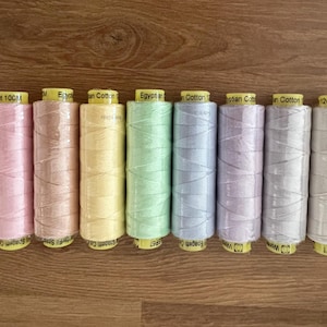 May include: Eight spools of colorful Egyptian cotton thread in pastel shades of pink, peach, yellow, green, blue, purple, gray, and white. Each spool is labeled with text and wrapped around a yellow core.