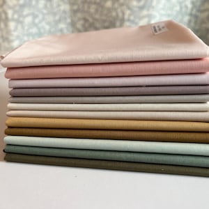May include: A stack of 10 fabric squares in various shades of pink, purple, gray, beige, brown, and green. The fabric is smooth and has a subtle sheen.