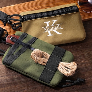 May include: A tan rectangular zippered pouch with the white embroidered letter K and the name Kenneth, paired with an olive green tactical pouch featuring black webbing, a metal pocket clip, and a coiled piece of tan rope attached to a black strap.