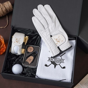 May include: A golf gift set in a black box containing a white golf glove, a white waffle-textured towel with a black embroidered golf ball and club logo with the name RICHARD, a white golf ball holder with tees, a golf ball, and a metal tool set.