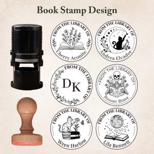 May include: A black self-inking stamp and a wooden handle stamp displayed alongside six circular book stamp designs featuring text reading From The Library Of and various illustrations including books, cats, a skull, and a globe.