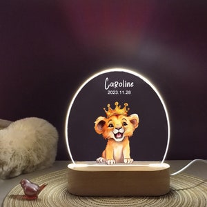 May include: A wooden night light with a clear acrylic circle featuring a cartoon lion cub wearing a gold crown. The circle is illuminated with white LED lights. The text "Caroline 2023.11.28" is printed on the acrylic circle.