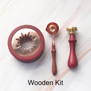 May include: A wooden kit for sealing wax, featuring a red wooden base with a copper snowflake design, a copper wax melting spoon, and a red wooden stamp with a gold top.