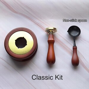 Peut inclure: Un kit de sceau de cire classique avec une base en bois, une t&ecirc;te de sceau en laiton et une cuill&egrave;re antiadh&eacute;sive. Le kit est sur une surface en marbre.