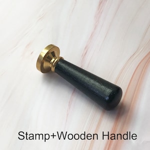 May include: A gold-toned wax seal stamp with a black wooden handle. The text "Stamp+Wooden Handle" is visible below the stamp.
