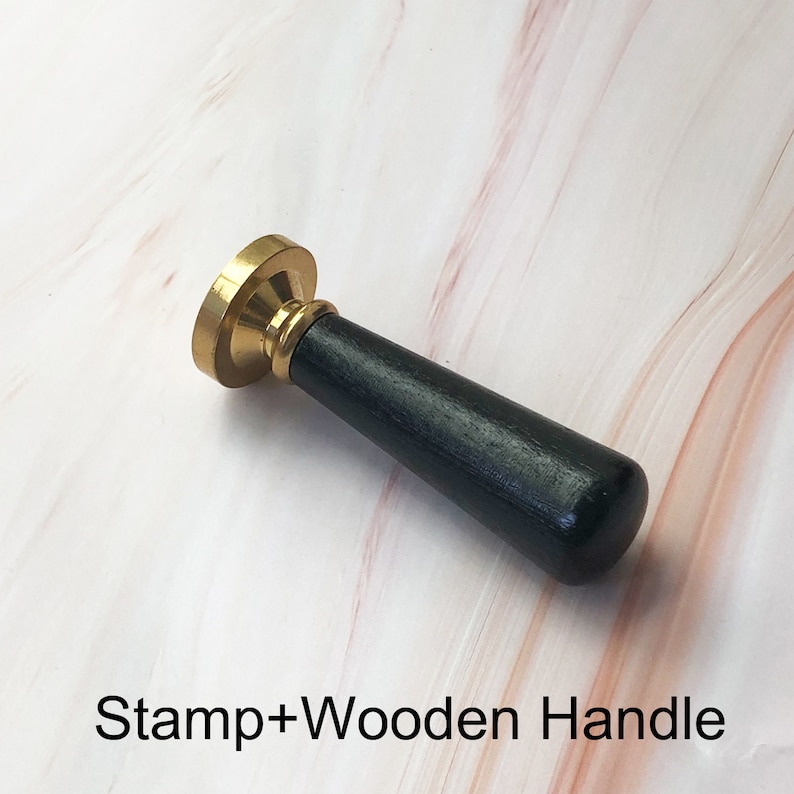 May include: A gold-toned wax seal stamp with a black wooden handle. The text "Stamp+Wooden Handle" is visible below the stamp.