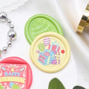 May include: A set of three colorful wax seals with birthday themes. The seals feature a cake, presents, and balloons. The text "Happy Birthday" is visible on one of the seals.