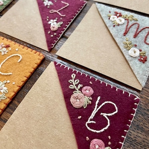 May include: A set of felt bookmarks with embroidered floral designs and letters. The bookmarks are in various colors, including green, brown, yellow, and red.