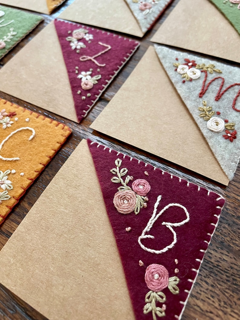 May include: A set of felt bookmarks with embroidered floral designs and letters. The bookmarks are in various colors, including green, brown, yellow, and red.