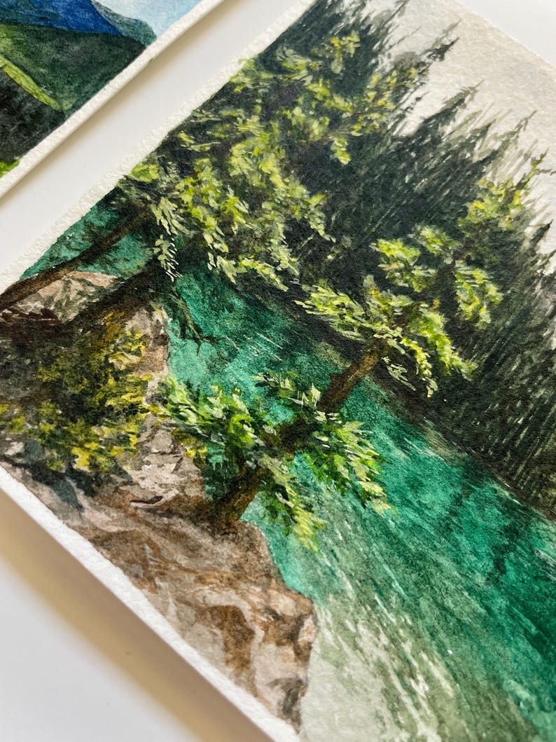 Peut inclure: Peinture &agrave; l'aquarelle d'un paysage pittoresque avec un lac turquoise et des arbres verdoyants. L'&oelig;uvre capture la beaut&eacute; naturelle d'une for&ecirc;t avec des coups de pinceau d&eacute;taill&eacute;s et une atmosph&egrave;re sereine. La peinture est sur papier textur&eacute;.
