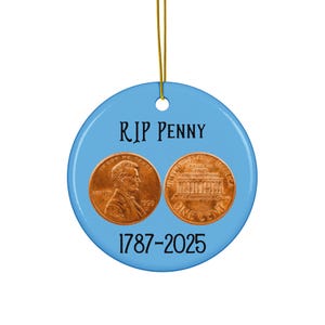 May include: A round, light blue ornament with the text "RIP PENNY" and the dates "1787-2025". The ornament features images of two US pennies. A gold string is attached for hanging.