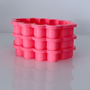 May include: A stack of four pink plastic cookie cutters shaped like a flower. The cutters are stacked on top of each other, with the top cutter being the largest and the bottom cutter being the smallest.