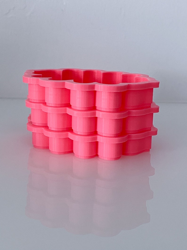 May include: A stack of four pink plastic cookie cutters shaped like a flower. The cutters are stacked on top of each other, with the top cutter being the largest and the bottom cutter being the smallest.