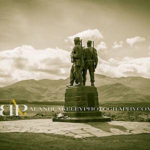 May include: A bronze statue of two soldiers standing back to back, facing a mountain range in the distance. The statue is on a stone pedestal and is surrounded by grass. The sky is cloudy and the image is in sepia tone.