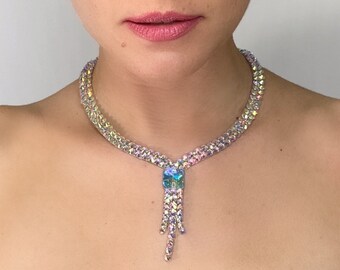May include: A woman wearing an iridescent crystal necklace with a teardrop pendant. The necklace is made of small, faceted crystals that sparkle in the light.