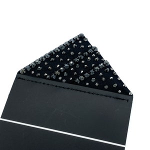 May include: Black fabric with a triangular section covered in black rhinestones. The fabric is folded over and stitched along the edge.
