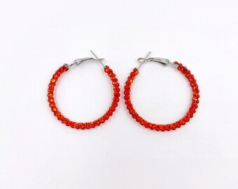 May include: A pair of orange hoop earrings with a beaded design. The earrings are made of metal and have a simple, elegant style.