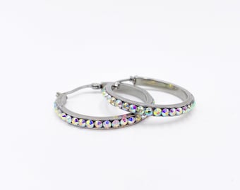 May include: A pair of silver hoop earrings with iridescent rhinestones around the edge.
