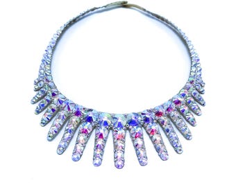 May include: A silver necklace featuring a row of iridescent crystals in a teardrop shape. The crystals are arranged in a cascading pattern, creating a dramatic and elegant look.