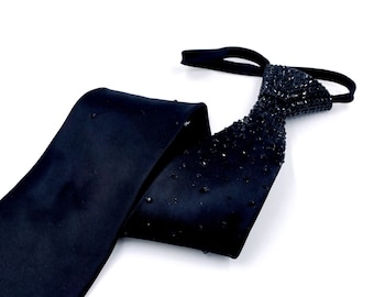 May include: A black satin tie with a black rhinestone embellishment. The tie is folded in half and the embellishment is on the front of the tie.