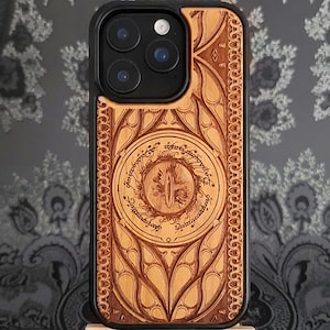 Op de afbeelding: Een houten telefoonhoesje met een zwarte rand. De hoes heeft een ingewikkeld lasergesneden ontwerp met een centraal oogmotief omringd door tekst. Het hout heeft een lichtbruine kleur.