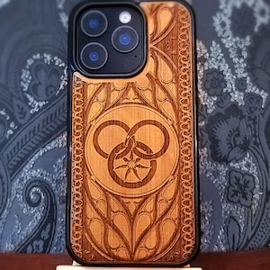 May include: A wooden phone case with a laser-cut design. The case has a black border and a detailed pattern of interlocking circles and floral elements. The wood has a warm, natural tone.