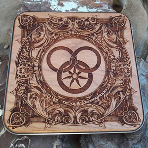 Puede incluir: Una placa de madera con un dise&ntilde;o intrincado y ornamentado. El centro presenta un s&iacute;mbolo estilizado de tres c&iacute;rculos entrelazados con una estrella en el centro.