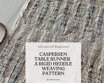 May include: A woven table runner with a textured, neutral color palette. The runner features a fringe at the bottom and a pattern of vertical stripes with blue and gray accents. Text on the image reads "CASPERSEN TABLE RUNNER A RIGID HEDDLE WEAVING PATTERN".