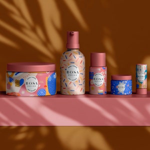 May include: A set of five colourful skincare products with a geometric pattern and the text "ROSA DESIGN ART STUDIO" on each. The products include a jar of cream, a bottle of lotion, a smaller bottle of serum, a jar of face mask, and a lip balm.