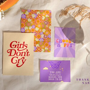 Puede incluir: Cuatro impresiones coloridas con mensajes inspiradores y un patr&oacute;n floral. Las impresiones tienen una est&eacute;tica retro de los a&ntilde;os 70 e incluyen el texto "Girls Don't Cry", "Choose Happy", "You Are Exactly Where You Need To Be", y "Thank You, Nassy".