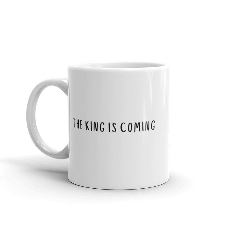 May include: White ceramic coffee mug with a black inscription that reads "THE KING IS COMING".