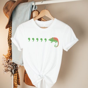 May include: White t-shirt with a green chameleon and five green quotation marks printed on the front.