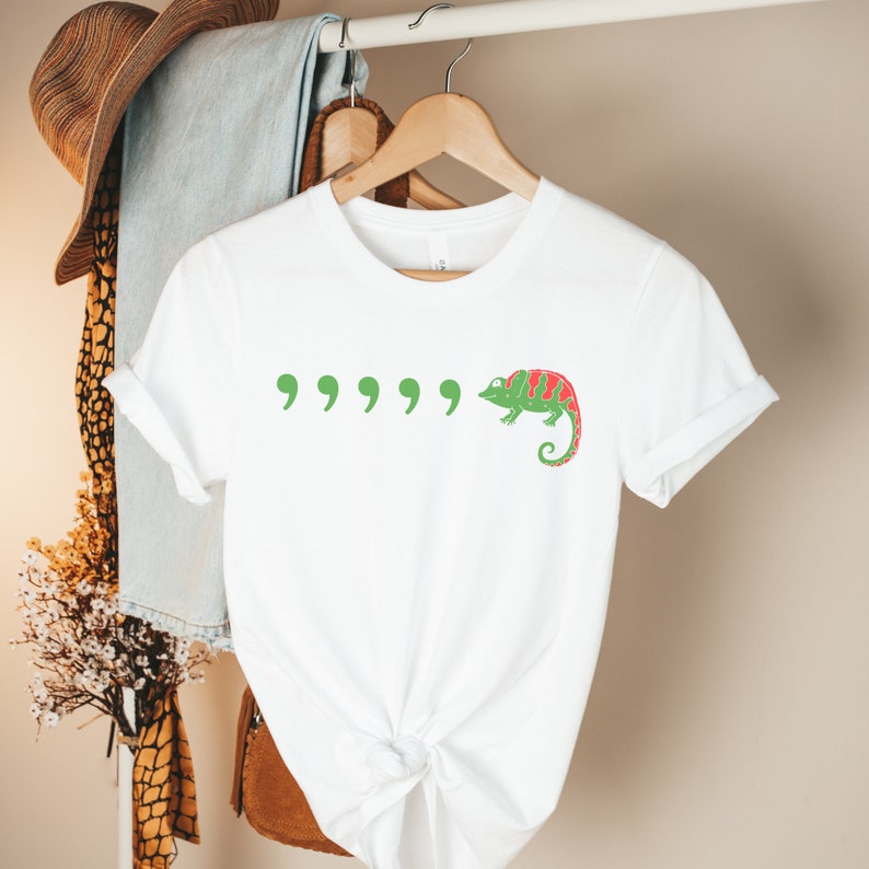 May include: White t-shirt with a green chameleon and five green quotation marks printed on the front.
