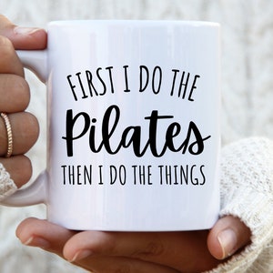 May include: White ceramic mug with black text that reads "First I do the Pilates then I do the things".