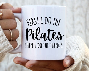 May include: White ceramic mug with black text that reads "First I do the Pilates then I do the things".
