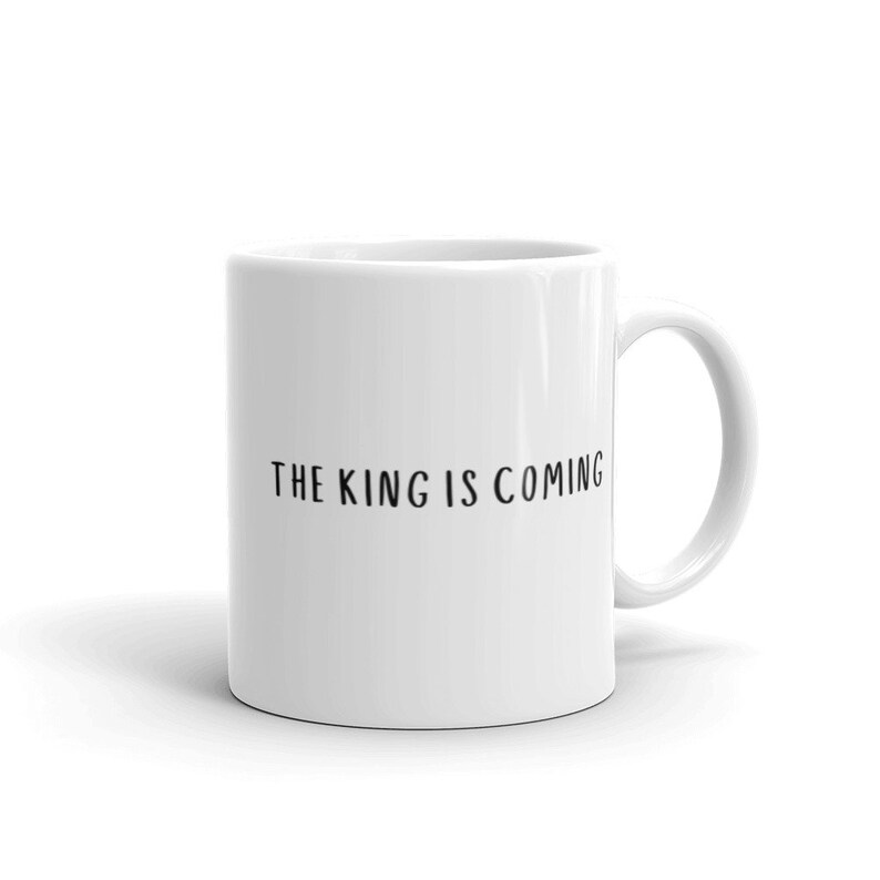 May include: White ceramic coffee mug with black text that reads "THE KING IS COMING".