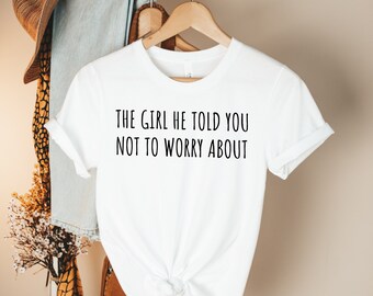 Puede incluir: Camiseta blanca con el texto "THE GIRL HE TOLD YOU NOT TO WORRY ABOUT" impreso en negro.