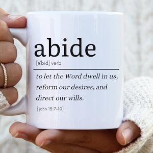Puede incluir: Taza de cerámica blanca con texto negro que dice "abide" y una definición de la palabra. La definición es "[ə'bid] verbo dejar que la Palabra habite en nosotros, reformar nuestros deseos y dirigir nuestras voluntades. [juan 15:7-10]"