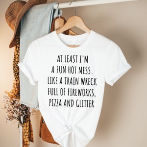 May include: White t-shirt with black text that reads "At least I'm a fun hot mess. Like a train wreck full of fireworks, pizza and glitter."
